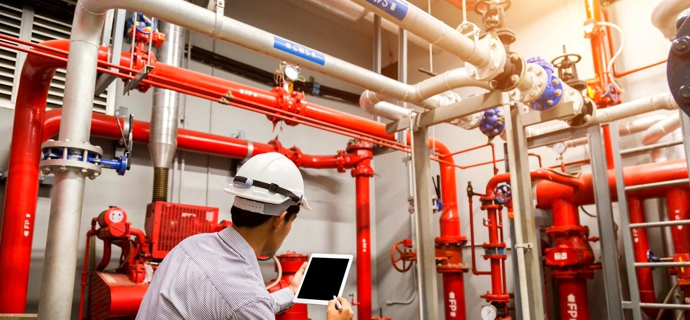 Técnico com tablet conferindo tubulação de incêndio em sala técnica, projeto de bombeiros (PPCI)